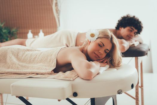 Young satisfied woman and man enjoying at the beauty salon, lying down and waiting for relaxing massage. 