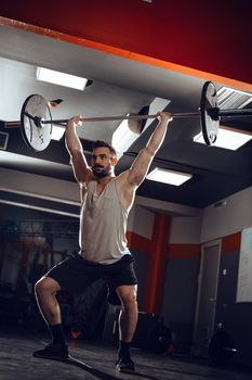 Young muscular man lifting a barbell at the gym. He doing overhead squat exercise with barbell on cross training.