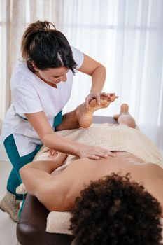 Handsome man lying down on massage table and getting healthy leg massage by young female therapist in the spa center.