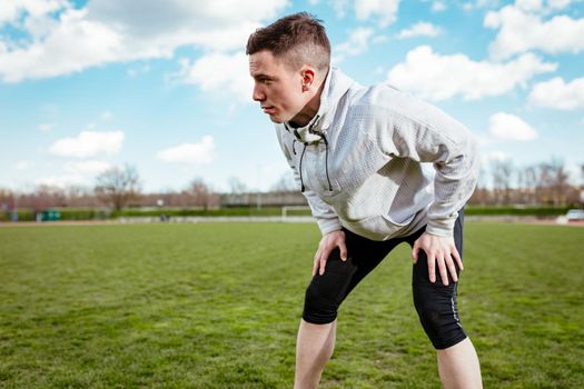 Urban jogger making pause during stretching and exercises in the training on empty stadium. 