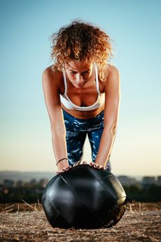 Young fitness woman doing push-ups on the wall ball in a sunset.