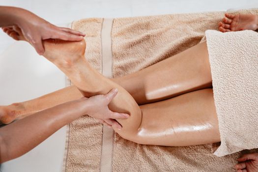 Close-up of a young female therapist massaging young woman's leg at beauty salon.