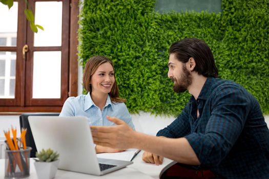 Young successful designers talking about project at the office. A man talking about project exposed on a laptop, and young woman listens her colleague and looking at him.
