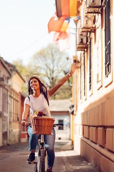 Happy woman riding the bike along the city street, in summer sunny day, smiling of joy during outdoor activity. 