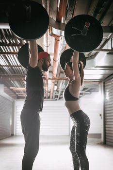 Young muscular couple doing snatch exercise with barbell on cross training at the garage gym.