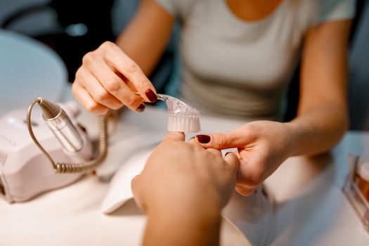 Close-up of a beautician hands brushing female clients nails after manicure process at the beauty salon.