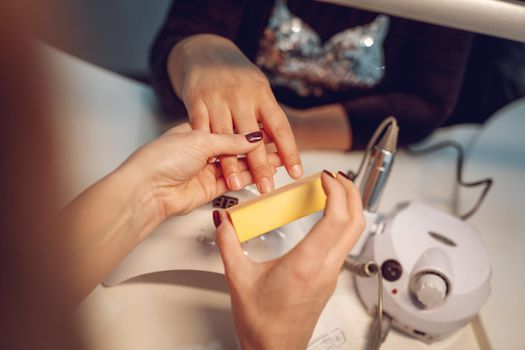 Close-up of a beautician hands polishing female clients nails with nail file at the beauty salon.