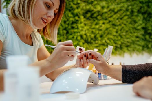 Happy beautician paint the nails of female clients at the beauty salon.