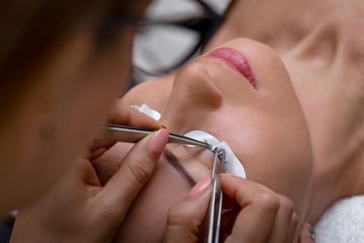 Close-up of a beautician hands applying extended eyelashes to model.  