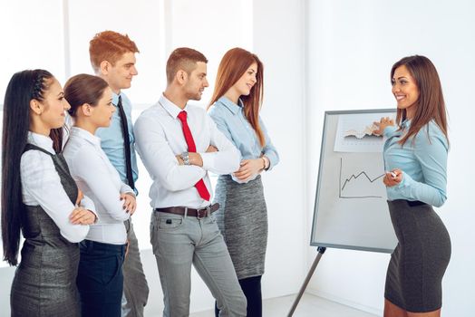 Businesspeople having meeting in a office. Young businesswoman standing in front of flip chart and having presentation.
