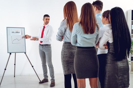 Businesspeople having meeting in a office. Young businessman standing in front of flip chart and having presentation.