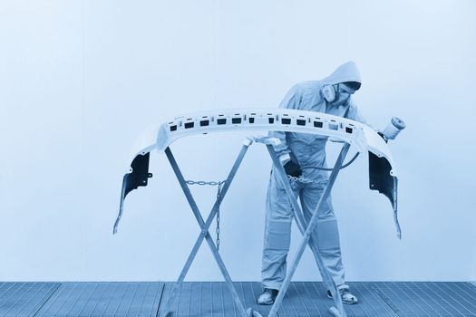 Mechanic painting bumper of a car with sprayer in painting booth