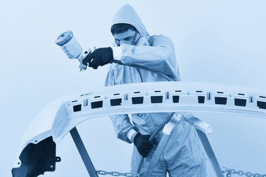 Mechanic painting bumper of a car with sprayer in painting booth