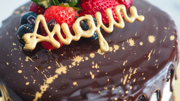 dark chocolate drips birthday sweet cake, fresh fruits Raspberry strawberry blueberry cranberry on top, decorated with golden edible paint