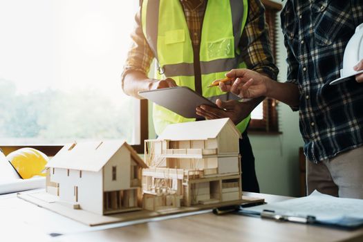 Engineers are consulting the team to design an architectural structure for clients with blueprints and building models to work at office.
