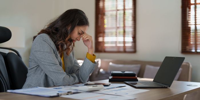 Stressed Asian business woman worry with many document on desk at office.