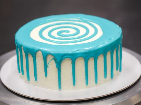pastry chef cake designer decorating turquoise blue white frosted cheesecake in kitchen with piping bag