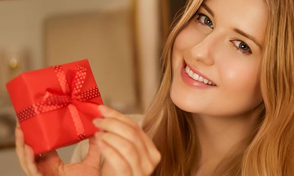 Surprised woman opening a gift and smiling in the evening at home, holidays and lifestyle.