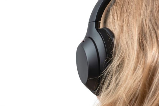 Woman in headphones isolated on white. Black headphones on a woman's head. Head of a fair-haired woman in headphones, rear view close-up