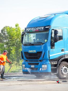 Man spraying exterior of blue semi truck using self service equipment at car wash.