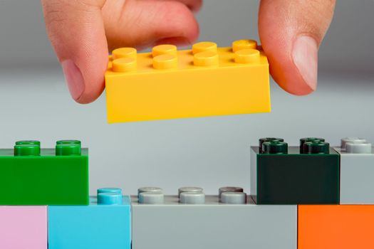 The child builds a tower of blocks. Toy building block in hand close-up. The concept of building and developing fine motor skills of hands.