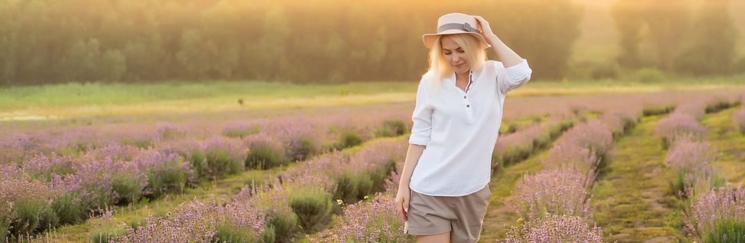 Young woman standing on a lavender field with sunrise on the background.