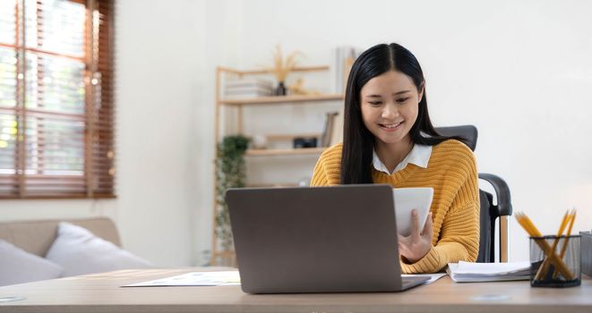 Portrait of Young Asian woman hand freelancer is working her job on computer tablet in modern home. Doing accounting analysis report real estate investment data, Financial and tax systems concept..