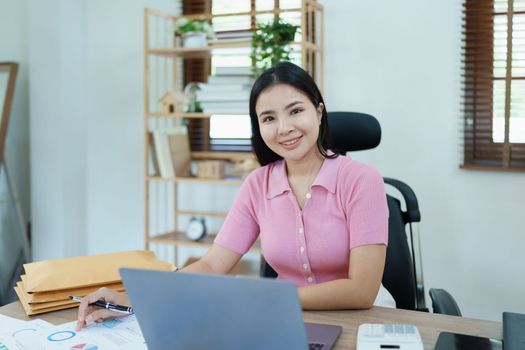 Portrait of a woman business owner showing a happy smiling face as he has successfully invested her business using computers and financial budget documents at work.