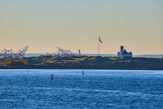 Image of Bayonne Golf Country Club in New York City from waters with industrial structures and American flag during soft sunset