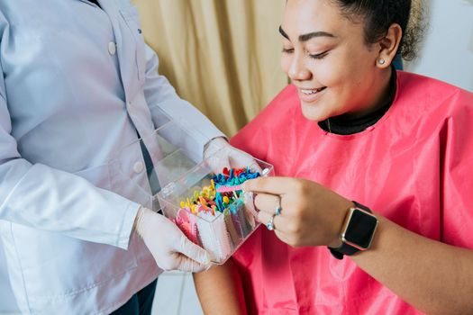 Female patient with dentist choosing dental braces, Smiling dental patient choosing dental braces, Patient with dentist choosing colored rubber band.