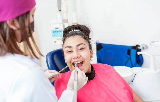 Stomatologist woman with drill cleaning patient girl mouth. Stomatologist drilling and cleaning a patient teeth, Woman stomatologist drilling patient teeth looking at the camera