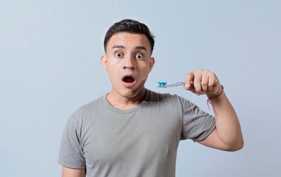 Amazed young man holding toothbrush with toothpaste isolated, guy with wow expression holding toothbrush isolated on white, Surprised young man holding a toothbrush with toothpaste