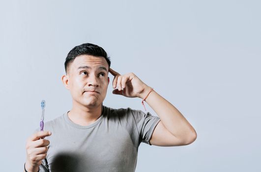 Man holding toothbrush with pensive expression isolated. Person holding toothbrush looking up, Thoughtful man holding toothbrush isolated, Portrait of young man thinking holding toothbrush
