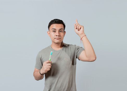Handsome guy holding toothbrush pointing an advertisement up. Caucasian handsome man holding toothbrush pointing up. People holding toothbrush pointing a promo up