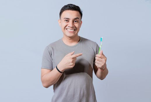 Handsome guy holding and pointing at toothbrush isolated. Person holding and pointing a toothbrush on isolated background, Smiling man holding and pointing at toothbrush