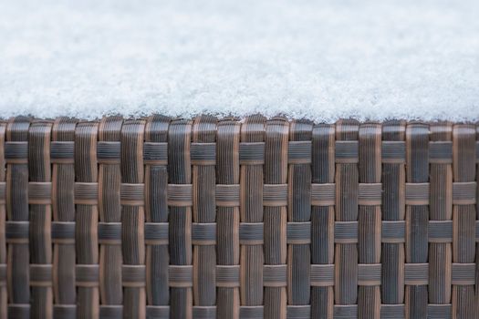 Care and storage of garden furniture in winter. texture of street furniture in winter. Artificial rattan covered with snow close-up