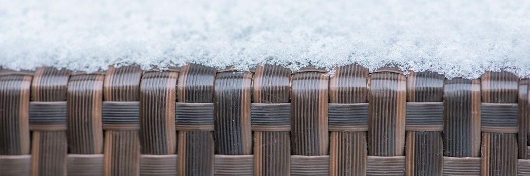 Care and storage of garden furniture in winter. texture of street furniture in winter. Artificial rattan covered with snow close-up