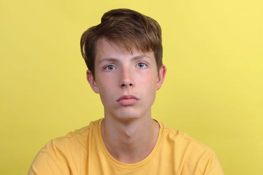 Beautiful thoughtful teenage boy on a yellow background close-up plan looks into the camera. Serious boy in a yellow T-shirt.