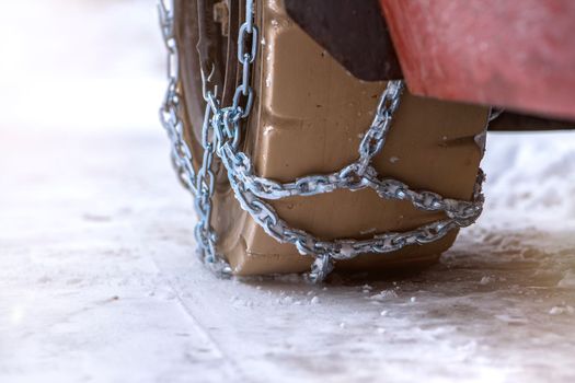 Wheel in the snow with safety and anti-skid chains. Loader or tractor with chains on wheels close-up. Driving safety in winter conditions.