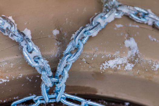 Wheel in the snow with safety and anti-skid chains. Loader or tractor with chains on wheels close-up. Driving safety in winter conditions.