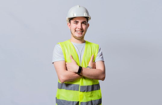 Portrait of smiling handsome engineer on white background, Portrait of young engineer wearing helmet and vest isolated. Young smiling engineer wearing helmet and vest with crossed arms isolated