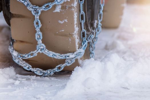 Wheel in the snow with safety and anti-skid chains. Loader or tractor with chains on wheels close-up. Driving safety in winter conditions.