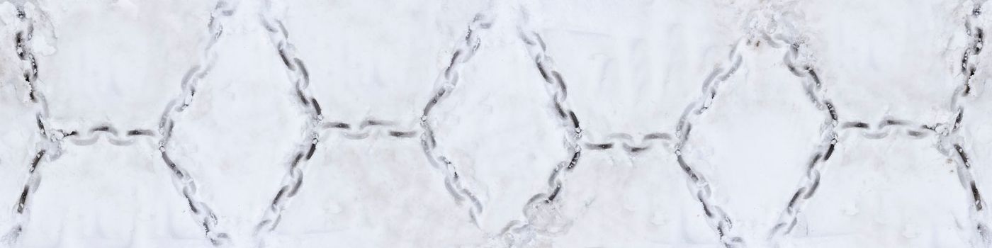 Tire texture on snow. Snow chain marks on an icy road. Track from the wheel of a car with a chain on the snow