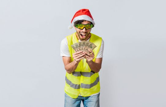 Builder engineer in christmas hat with happy expression holding dollars isolated. Concept of engineer with money in holiday season, Engineer in christmas hat holding money smiling at camera