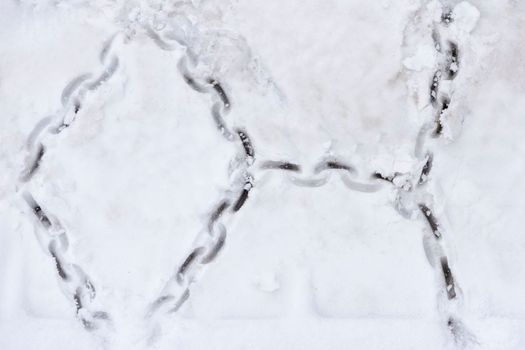 Tire texture on snow. Snow chain marks on an icy road. Track from the wheel of a car with a chain on the snow