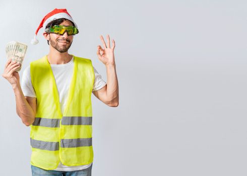 Engineer in christmas hat holding money in ok gesture. builder engineer in christmas hat with approving expression holding money bills. Christmas engineer concept holding money in happy holidays