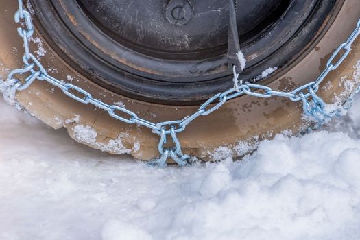 Wheel in the snow with safety and anti-skid chains. Loader or tractor with chains on wheels close-up. Driving safety in winter conditions.