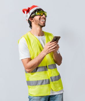 Happy Engineer in christmas hat using cell phone isolated. Smiling engineer in christmas hat using cell phone. Concept of engineer with christmas hat laughing while using cell phone at christmas