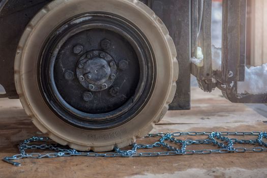 The process of installing an anti-skid chain on a wheel in winter. Preparing a loader, tractor or truck for a snowy road. Snow chains close up.