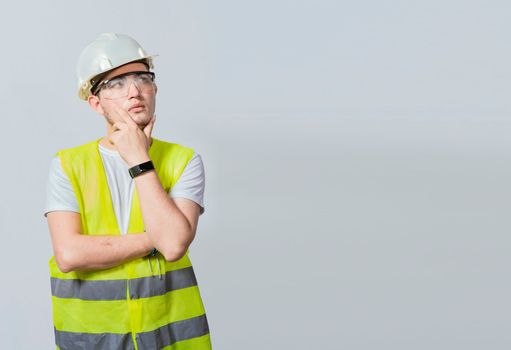 Concept of a meditative engineer solated. Pensive builder man with hand on chin, Portrait of young builder thinking with hand on chin isolated, A pensive engineer on white background